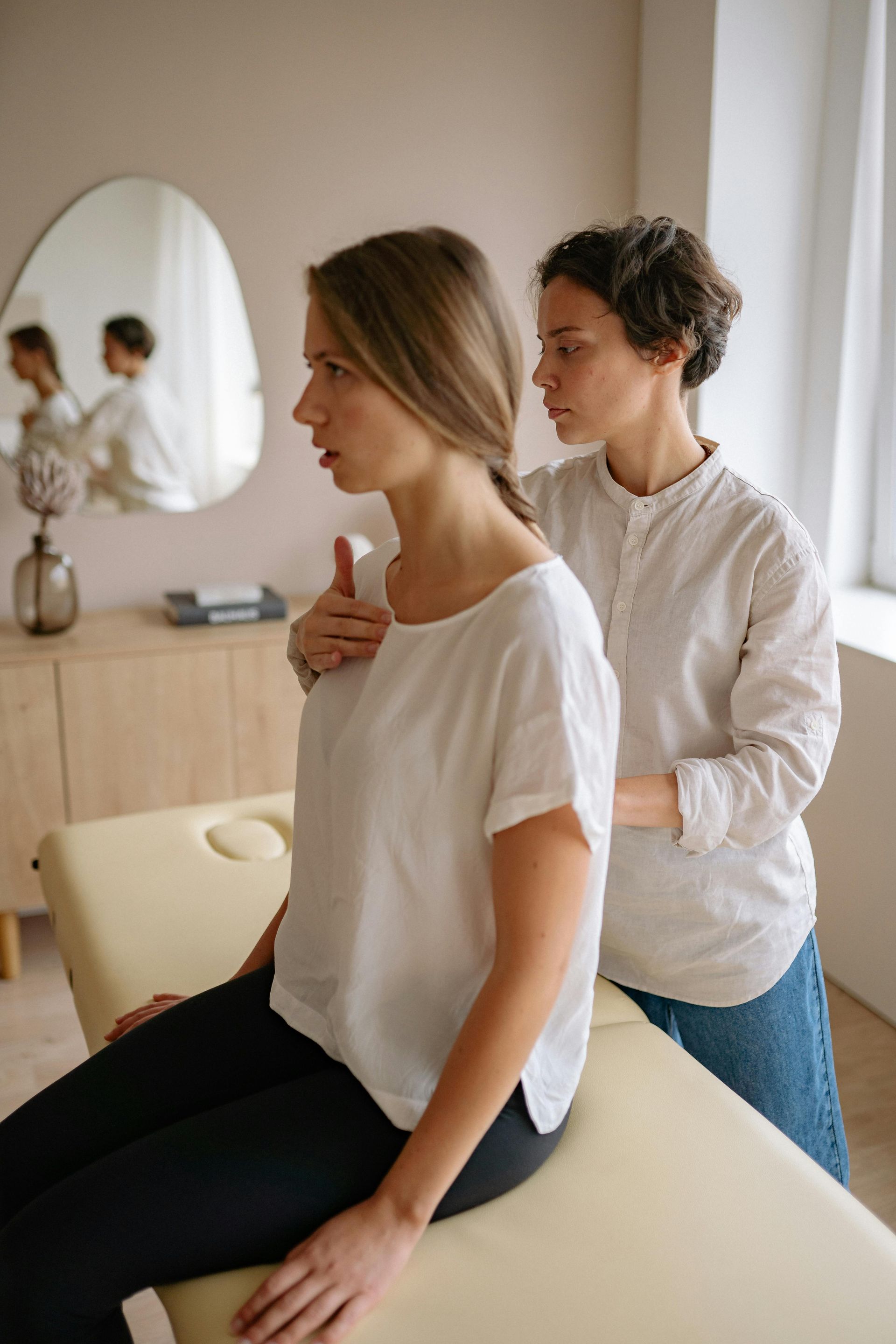 Two therapists in white shirts tending to a client on a massage table in a bright clinic room