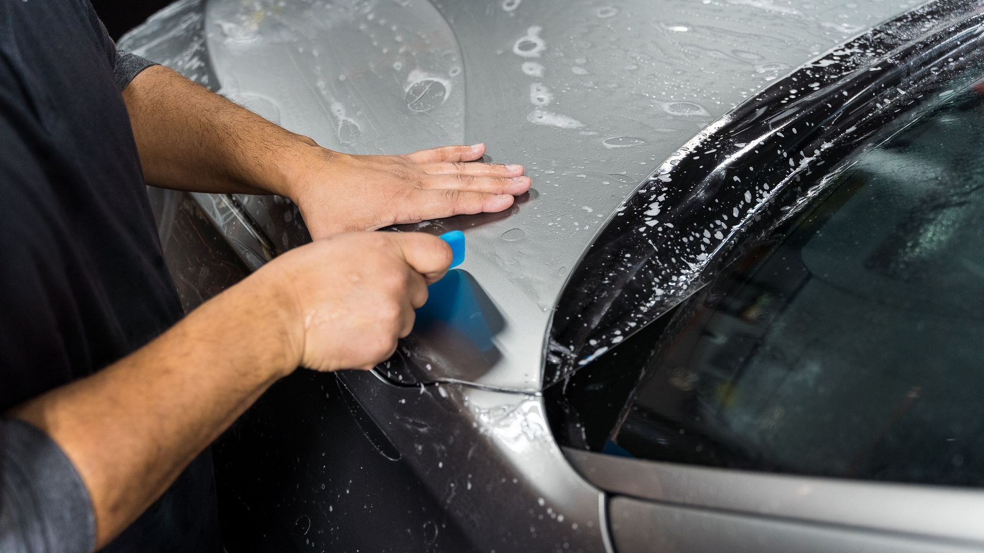 A man is applying a protective film to the hood of a car .