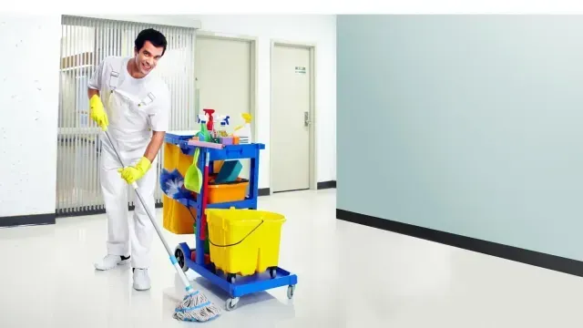 Un hombre está limpiando el piso con un trapeador y un carrito.