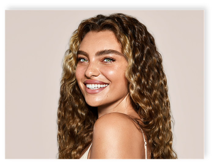 A woman with curly hair is smiling and looking over her shoulder.