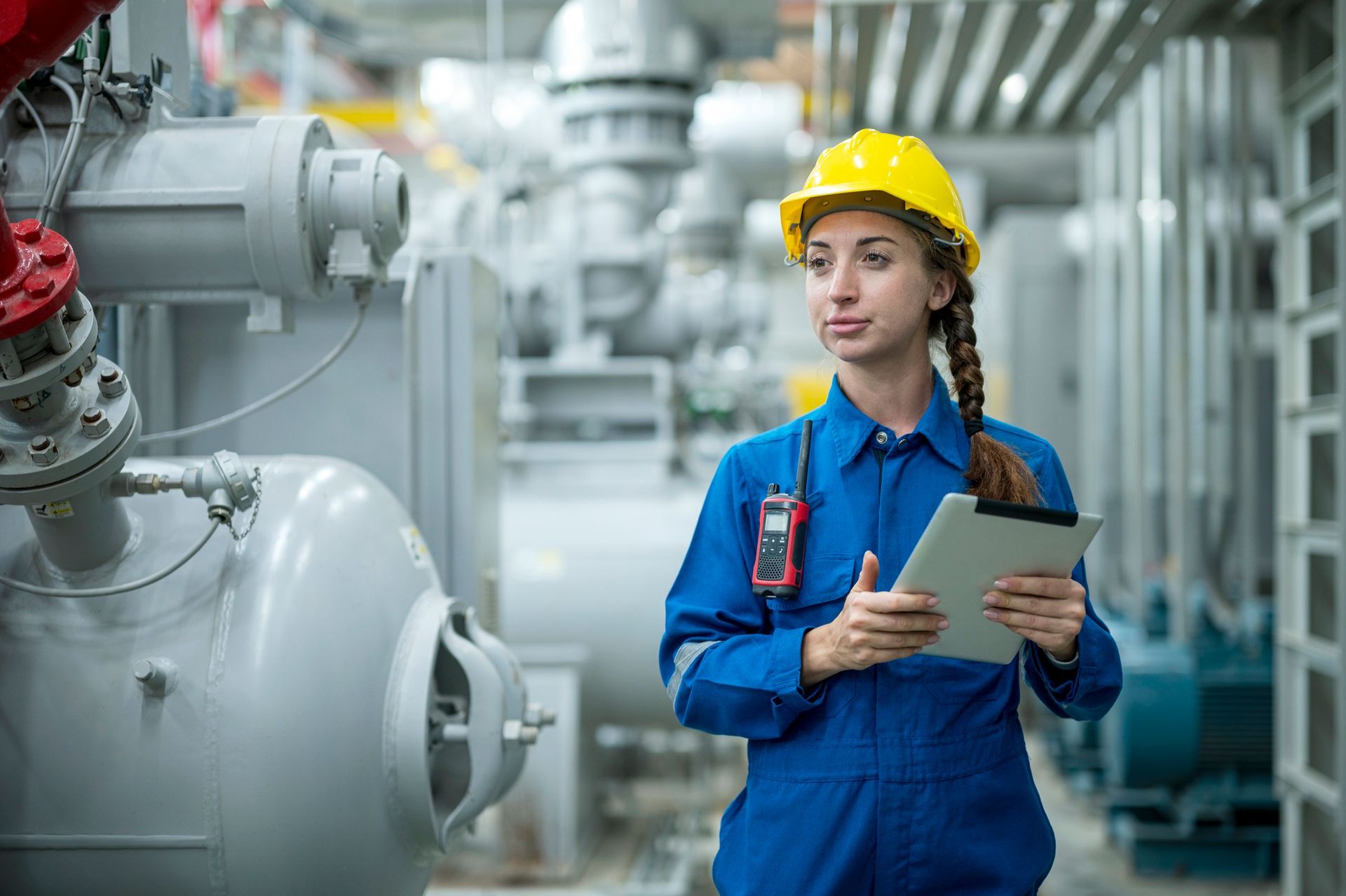 Female stationary engineer working at industrial mechanical room, examining the operation of the ven