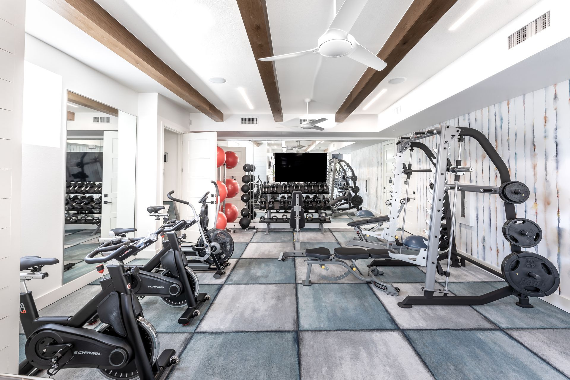 A large gym with a lot of exercise equipment and a flat screen tv at The Bennett, which offers apartments in South Austin, TX.
