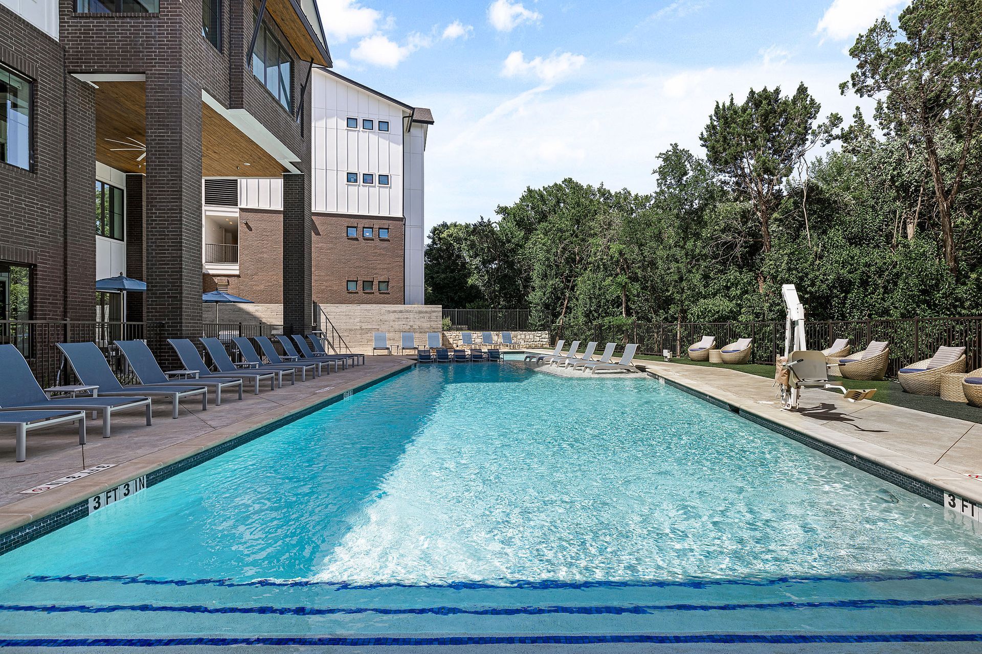 A large swimming pool surrounded by chairs and trees in front of an apartment building in South Austin.