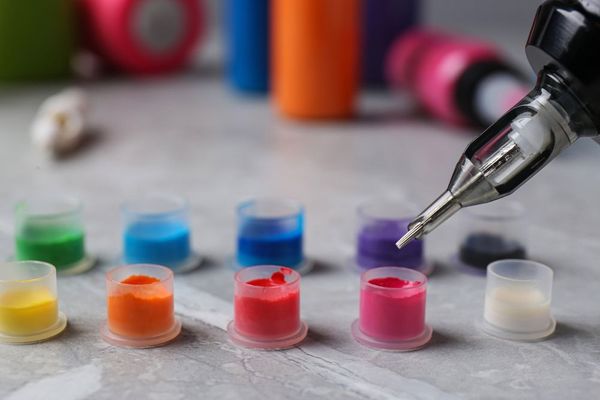 A close up of a tattoo machine and bottles of ink on a table.