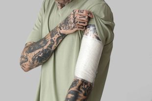 A man with tattoos is holding his arm with a bandage on it.