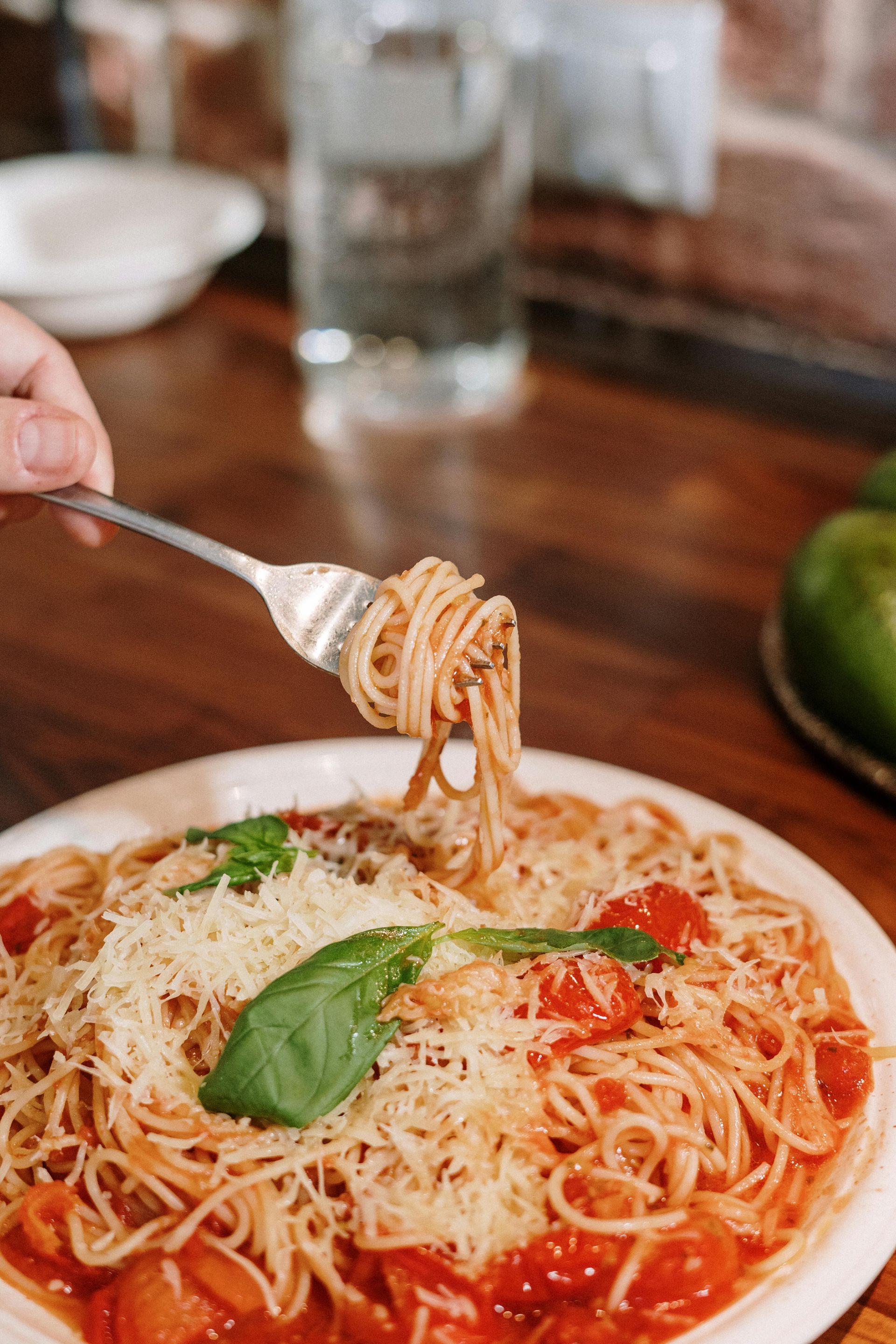Fork lifting spaghetti from a plate of red sauce with basil on a restaurant table