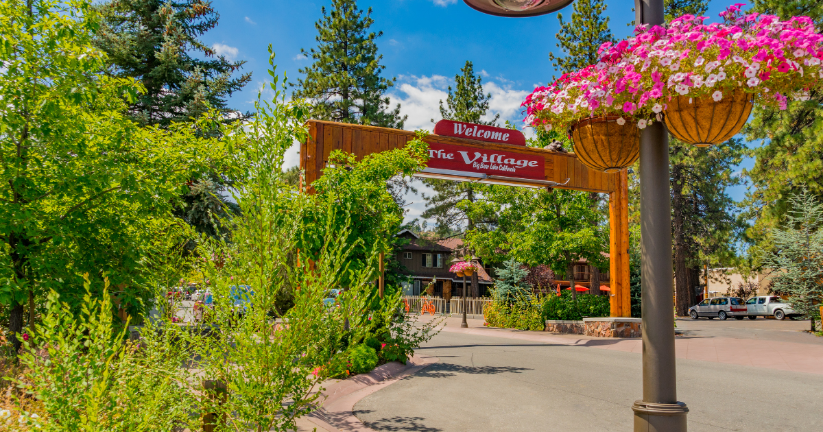 Entrance sign to the Village in Big Bear Lake on a pole with flowers hanging from it.