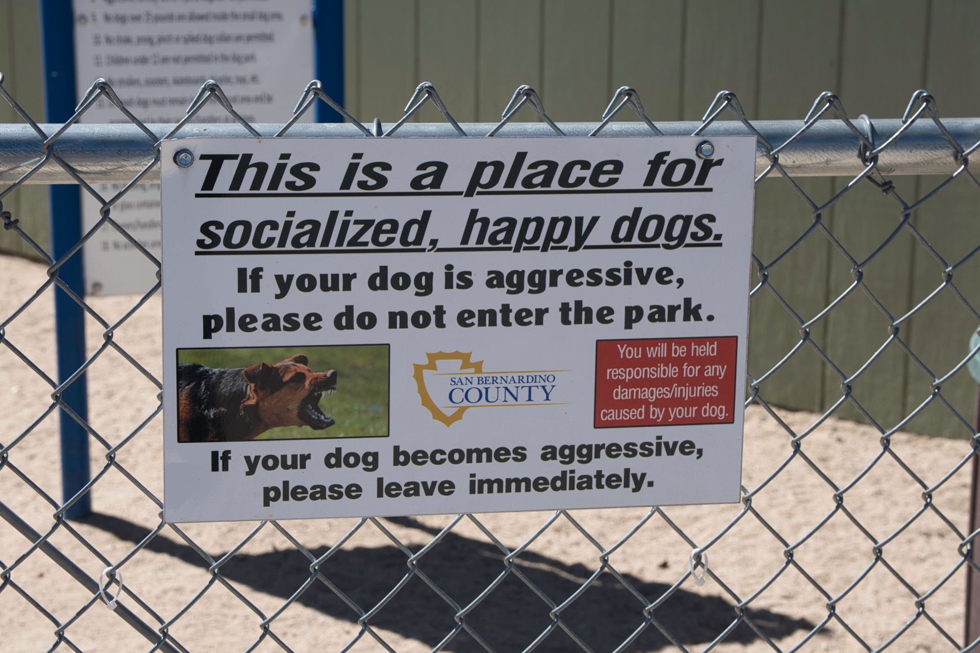 A sign on a chain link fence at Bark Park in Big Bear Lake that says this is a place for socialized happy dogs