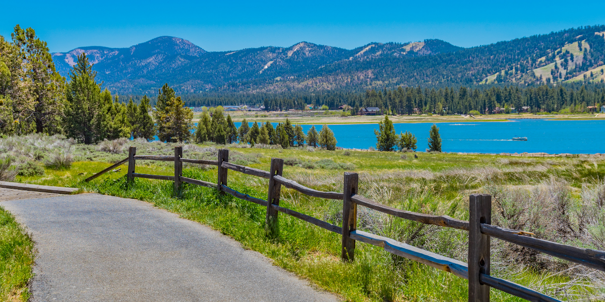 Alpine Pedal Path with a wooden fence leading to a lake with mountains in the background.