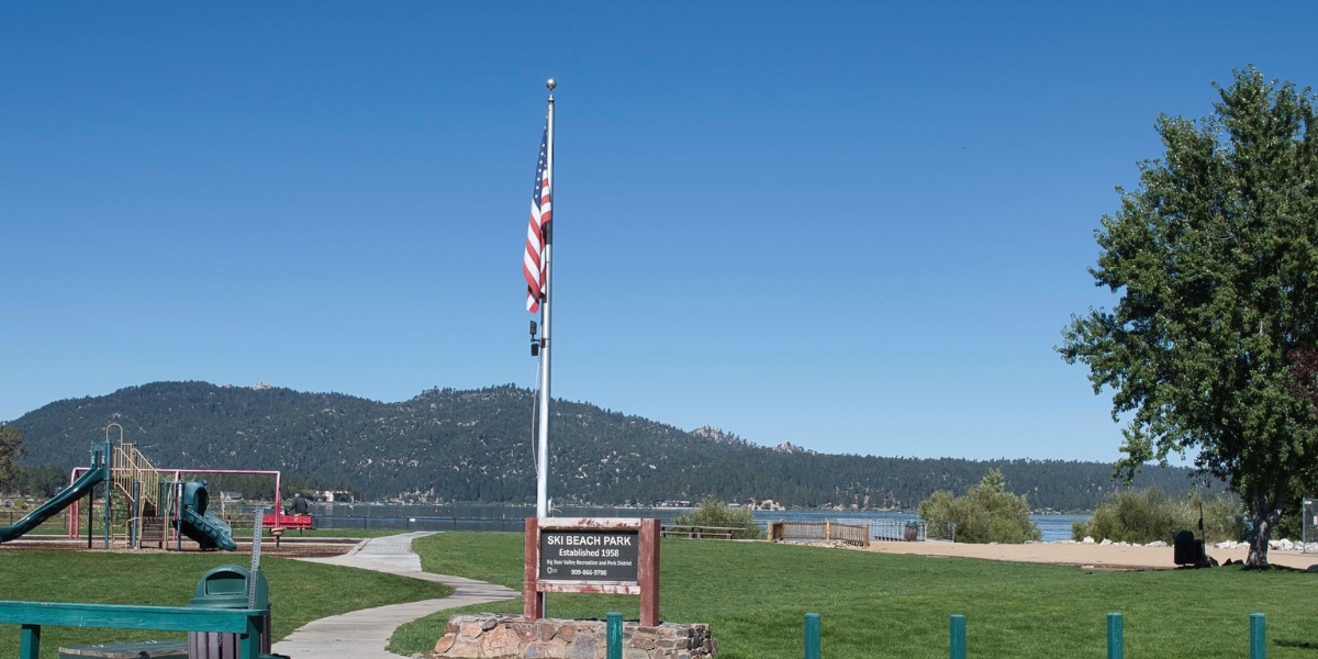 An american flag is flying in at Ski Beach Park in Big Bear Lake with mountains in the background