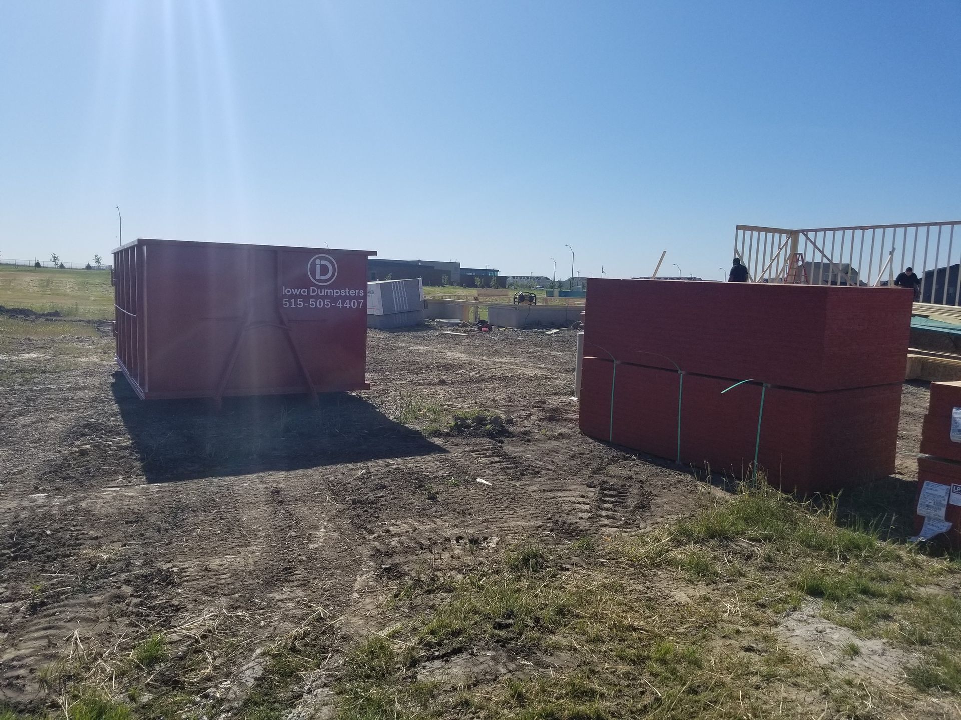 Two stacks of red building materials sit on a grassy construction site under a bright blue sky.