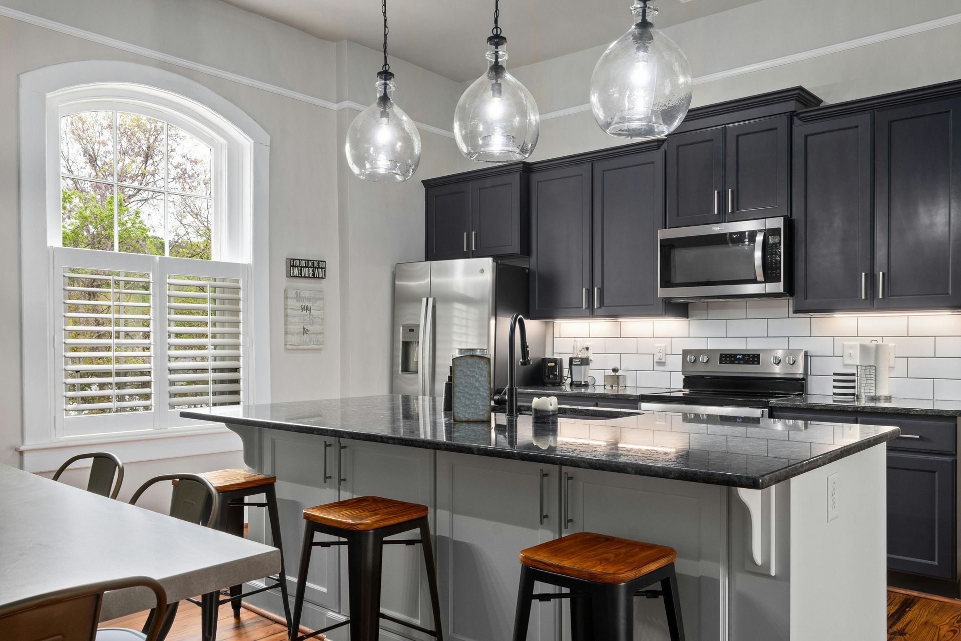 A kitchen with black cabinets , stainless steel appliances , a large island , a table and chairs.