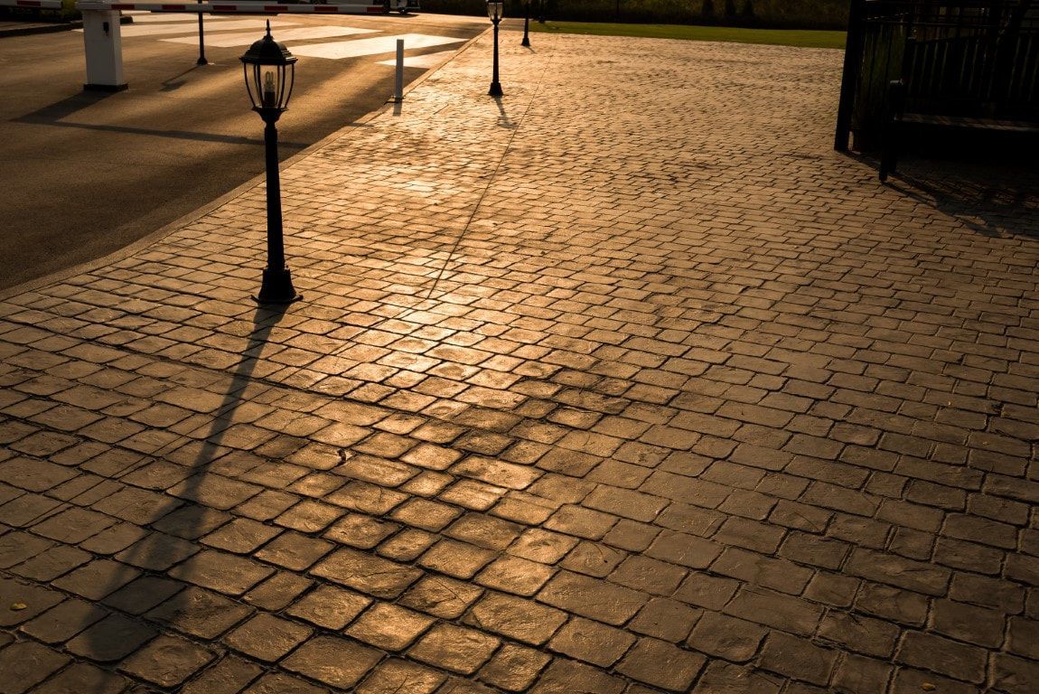 Sunset casts long shadows of street lamps on a cobblestone path, creating a warm, tranquil, and inviting atmosphere.