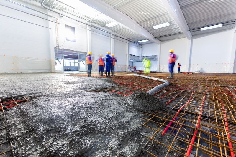 Workers in safety gear and helmets pour and level concrete on a rebar grid in a large.