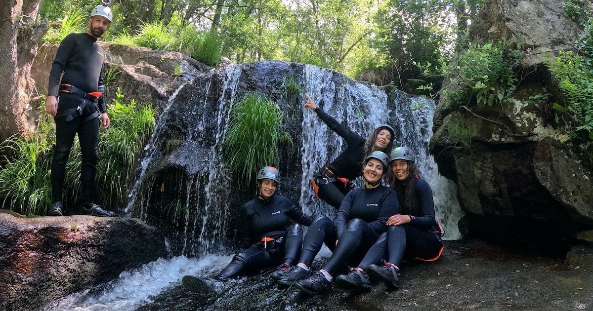 grupo e amigas divertem-se numa actividade de trekking aquático junto a uma cascata 