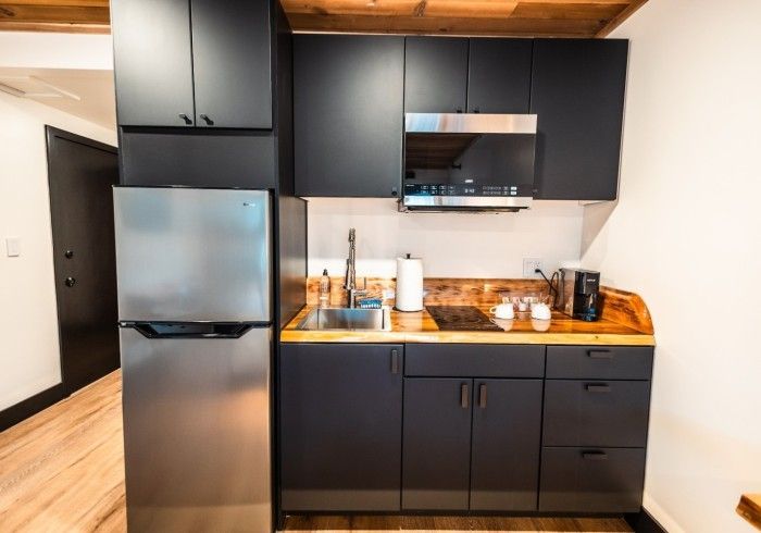 A kitchen with black cabinets , a stainless steel refrigerator , a sink , and a microwave.