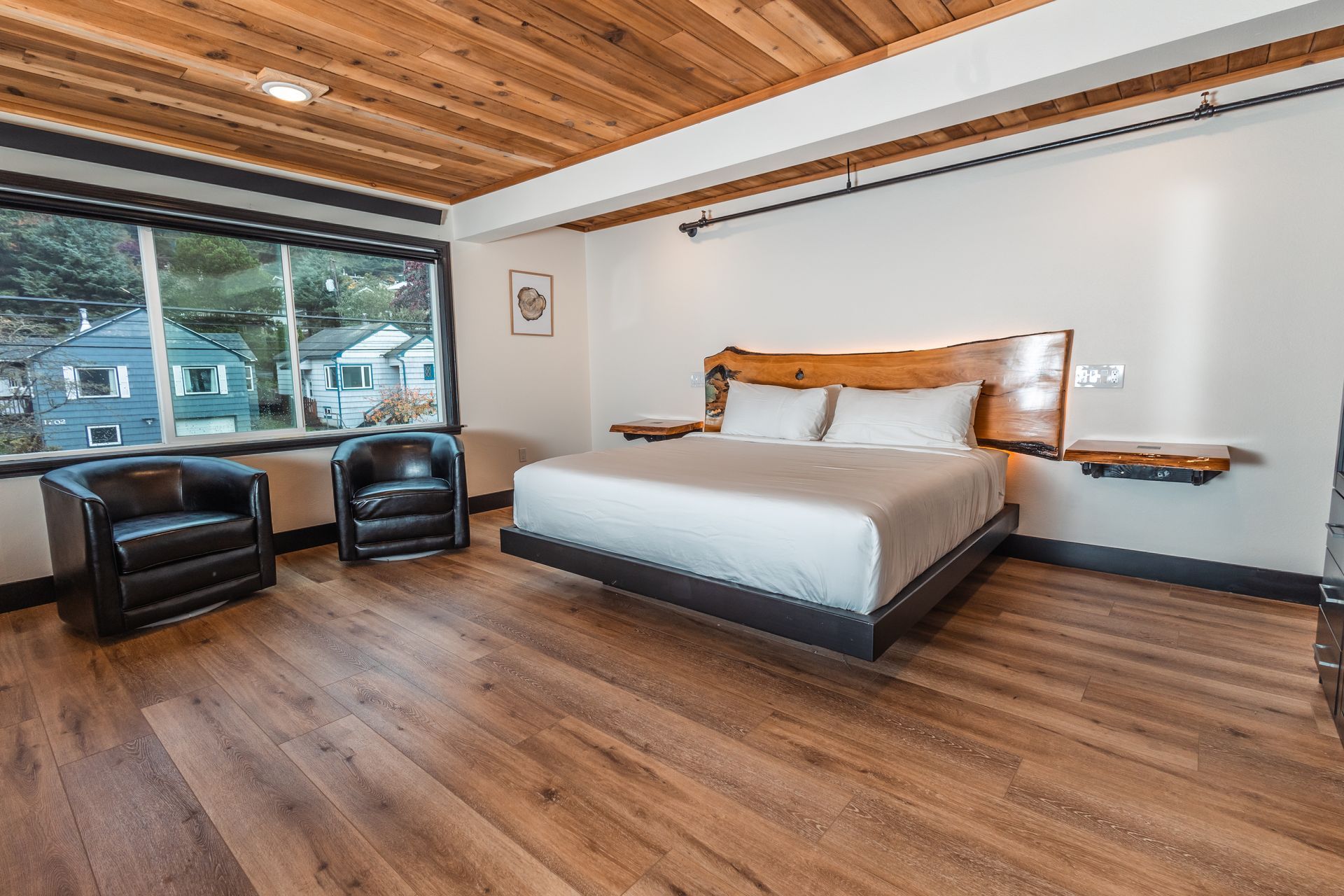 A hotel room with a king size bed , two chairs and a large window.