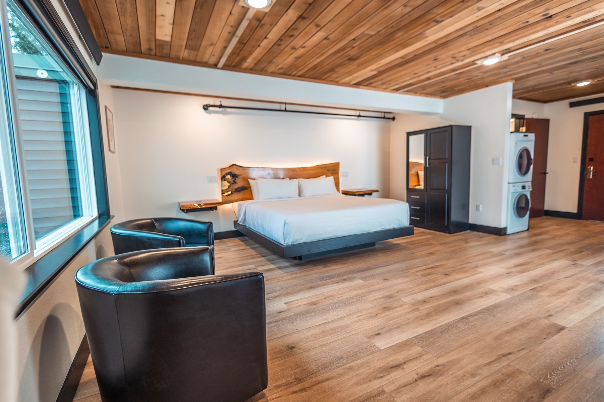 A hotel room with a king size bed , two chairs and a washer and dryer.