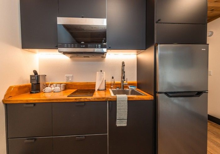 A kitchen with stainless steel appliances , black cabinets , a sink , and a refrigerator.