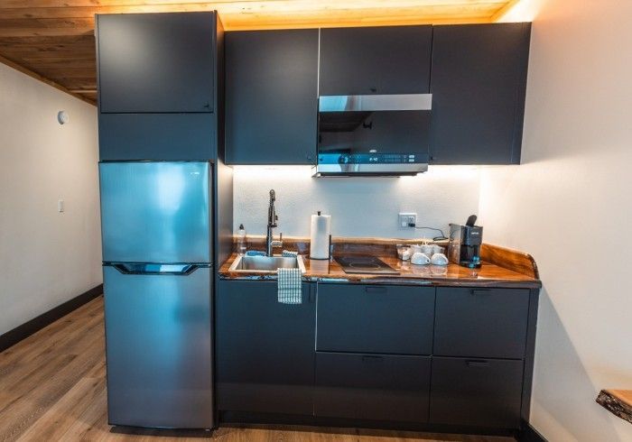 A kitchen with black cabinets and a stainless steel refrigerator