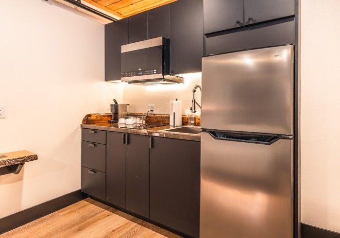 A kitchen with stainless steel appliances , black cabinets , a sink and a refrigerator.