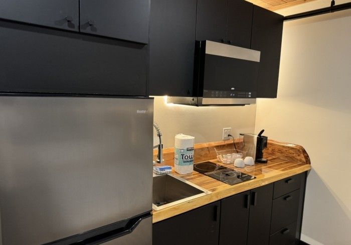 A kitchen with black cabinets , a stainless steel refrigerator , a sink , and a microwave.