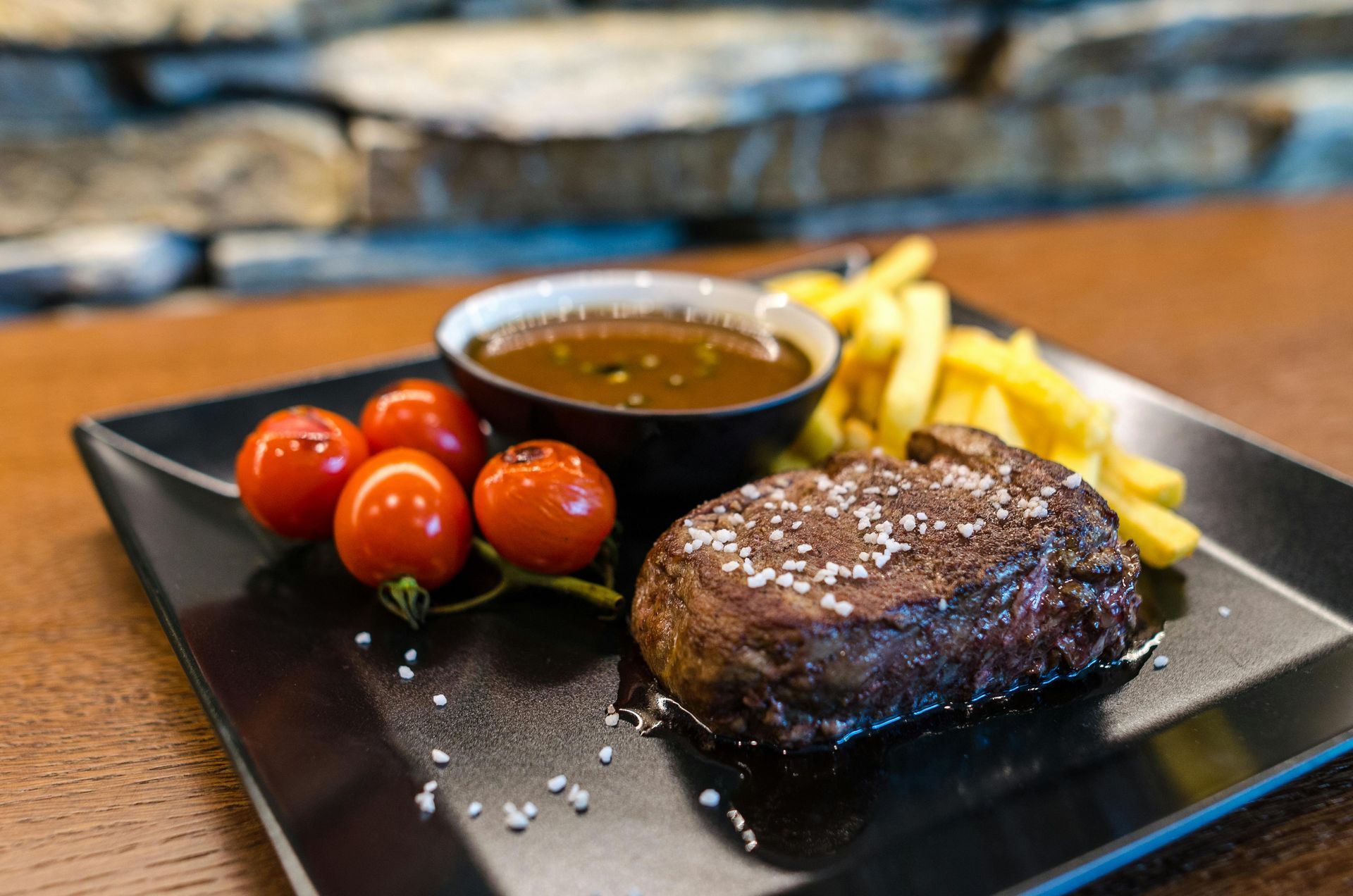 A black plate topped with a steak , french fries and tomatoes.