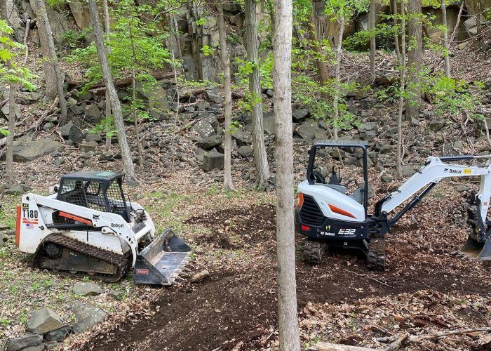 A bulldozer and an excavator are parked in the woods.