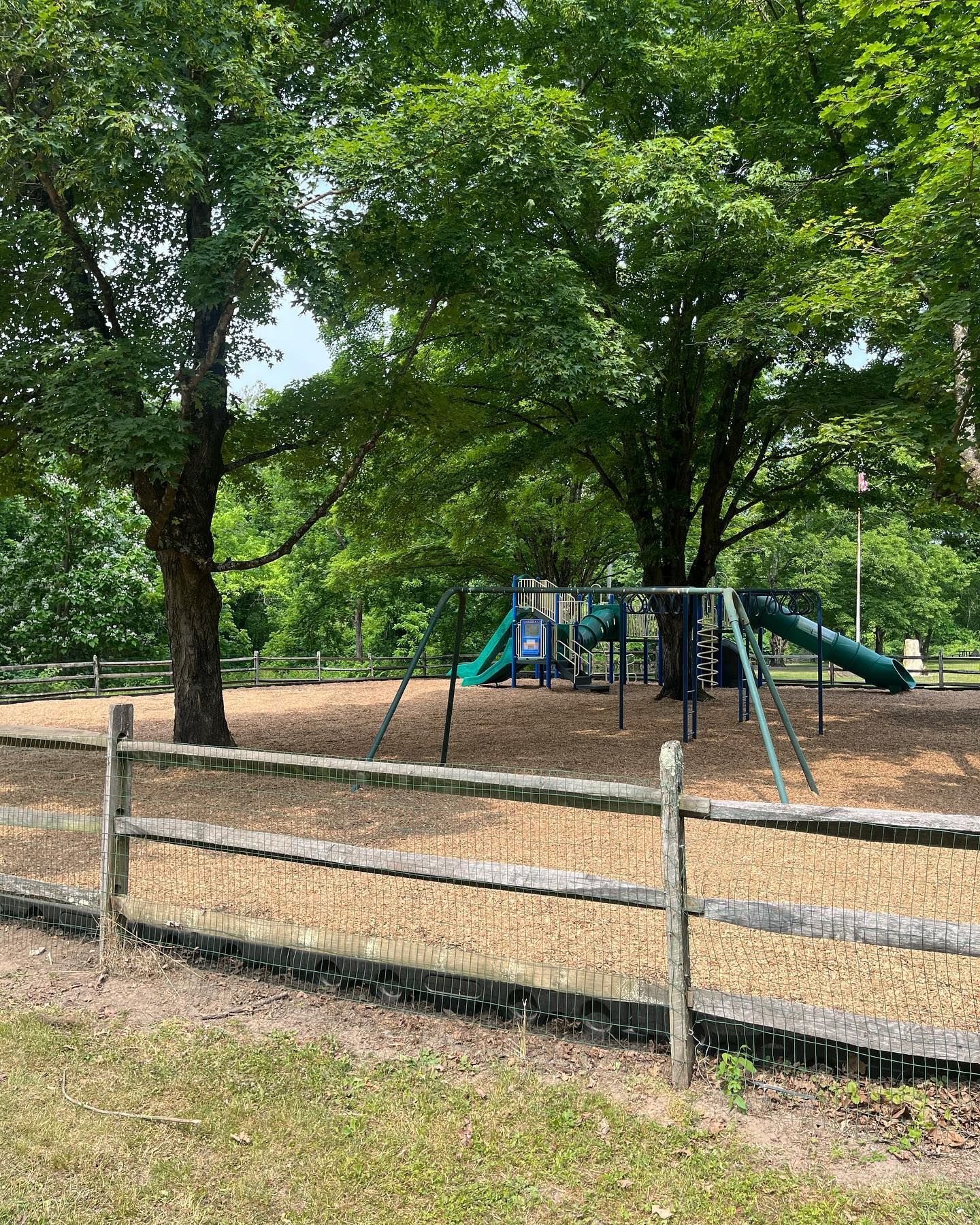 A wooden fence surrounds a playground in a park.
