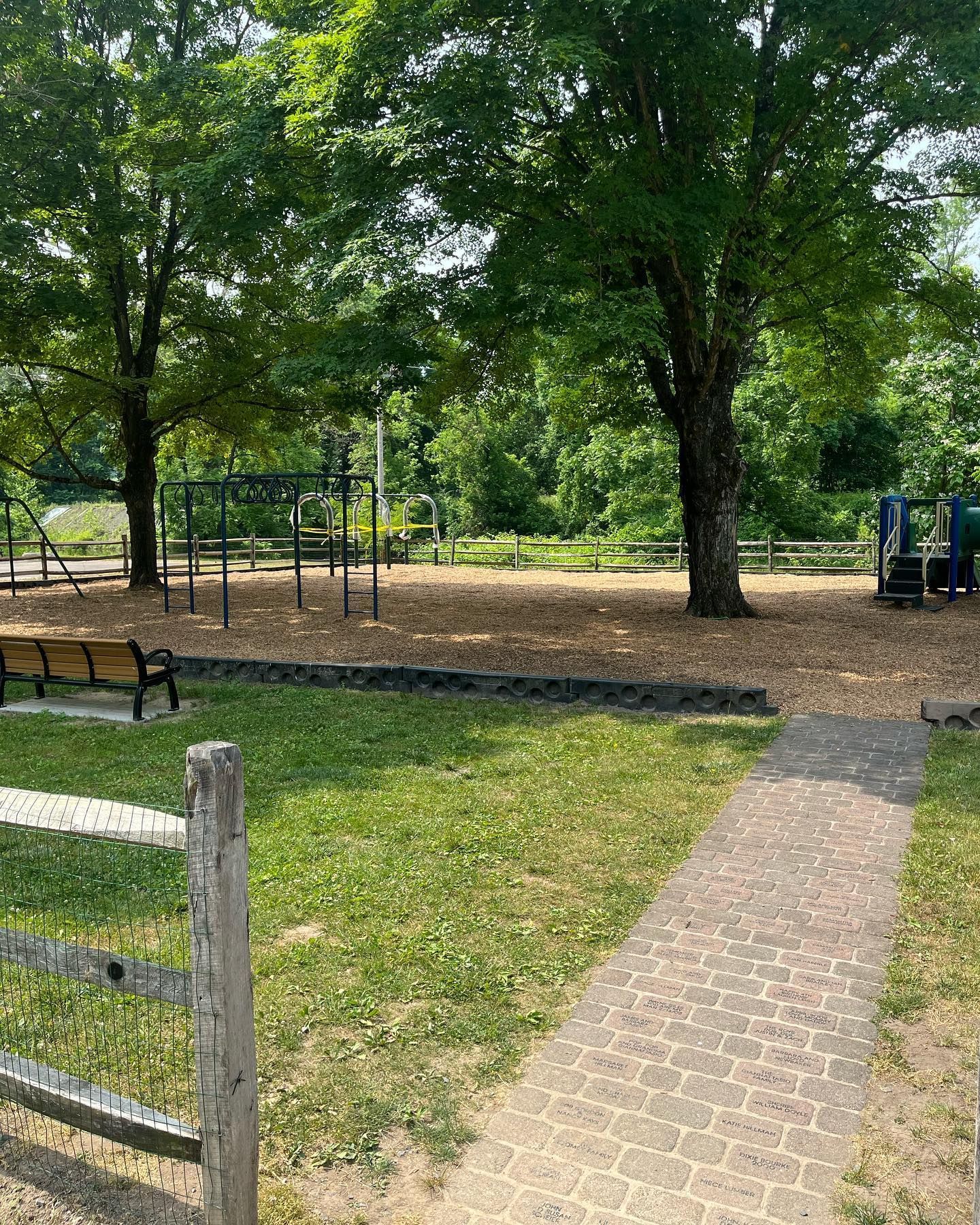 A brick walkway leading to a playground in a park.