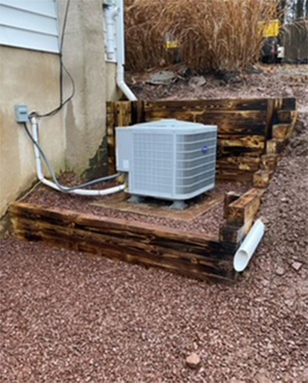 A white air conditioner is sitting on a wooden platform next to a house.