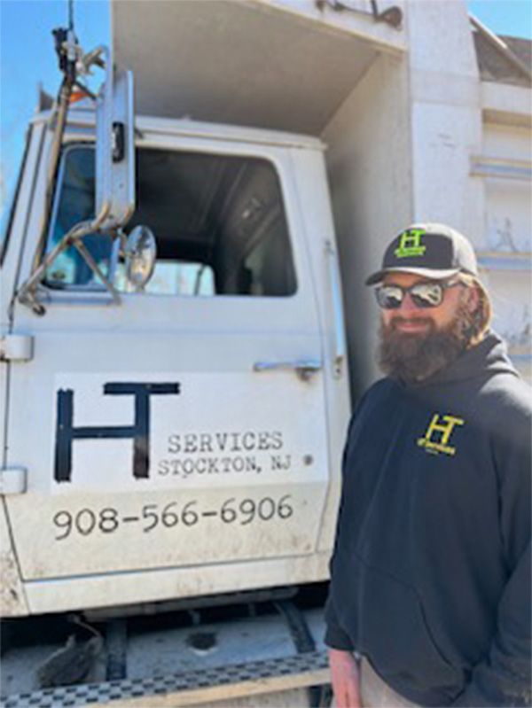 A man with a beard is standing in front of a truck that says services stockton nj