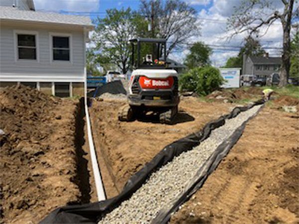 A bobcat is driving down a dirt road next to a house.