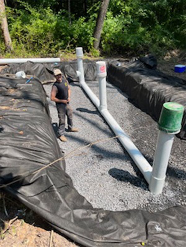 A man is standing next to a pile of pipes in the dirt.
