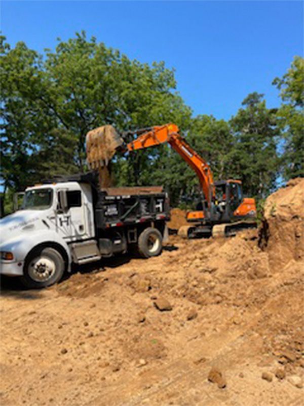 A dump truck is being loaded with dirt by an excavator.