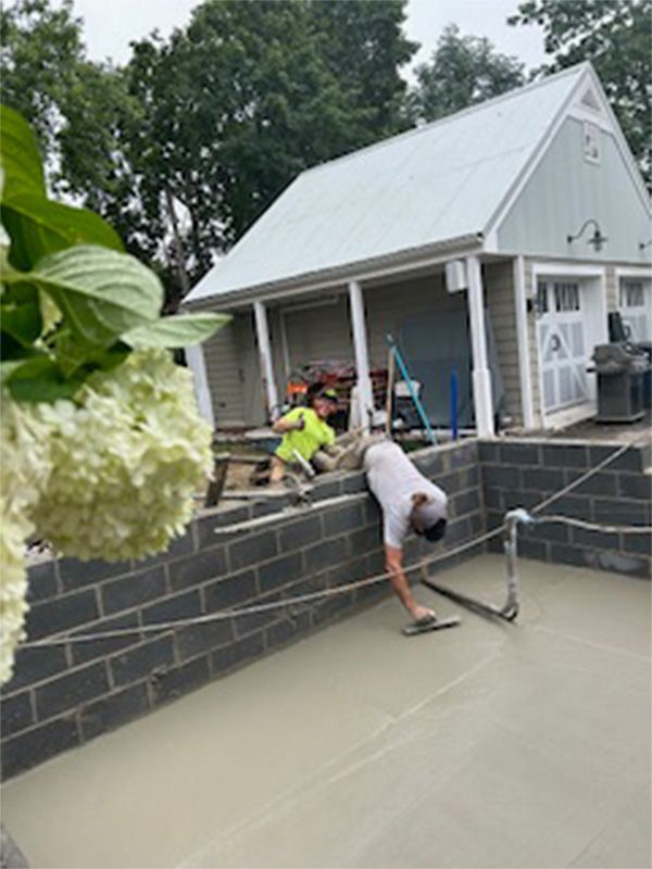 A man is laying concrete on a brick wall in front of a house.