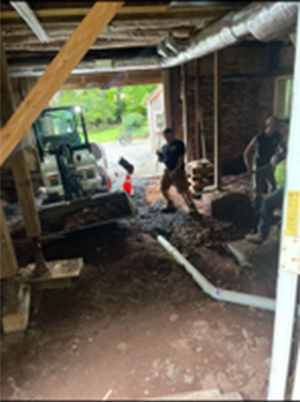 A man is digging in a basement with a tractor in the background