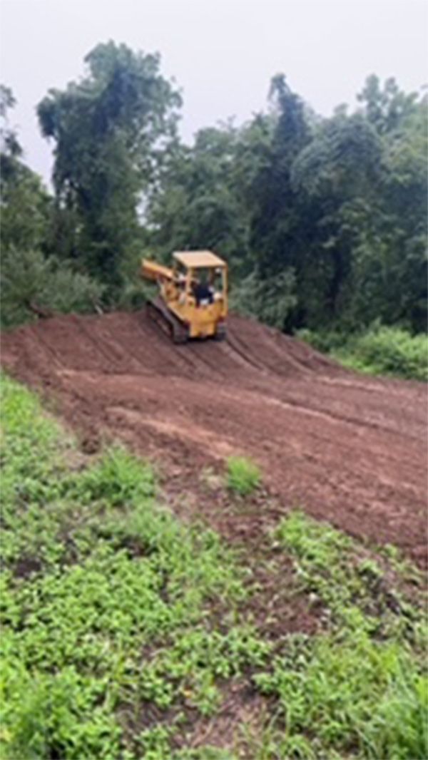 A bulldozer is driving down a dirt road in a field.