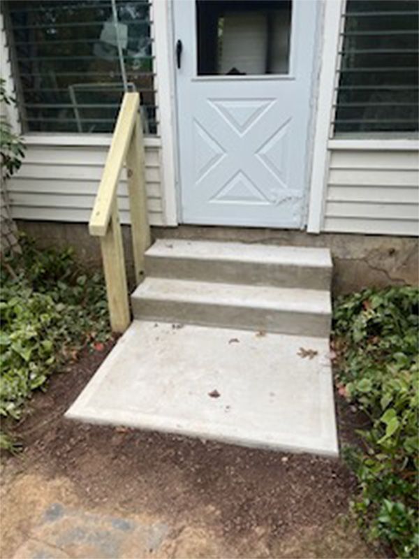 A set of concrete steps leading up to a door with a wooden railing.