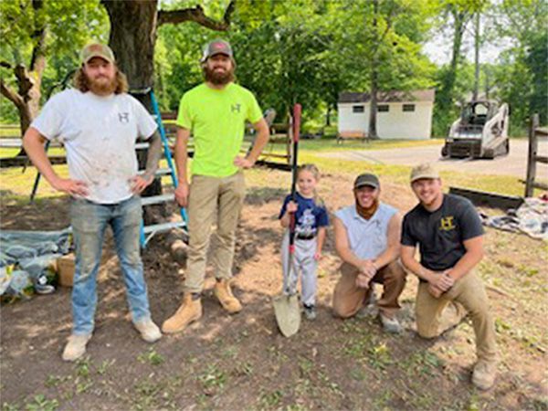 A group of men are posing for a picture with a little boy holding a shovel.