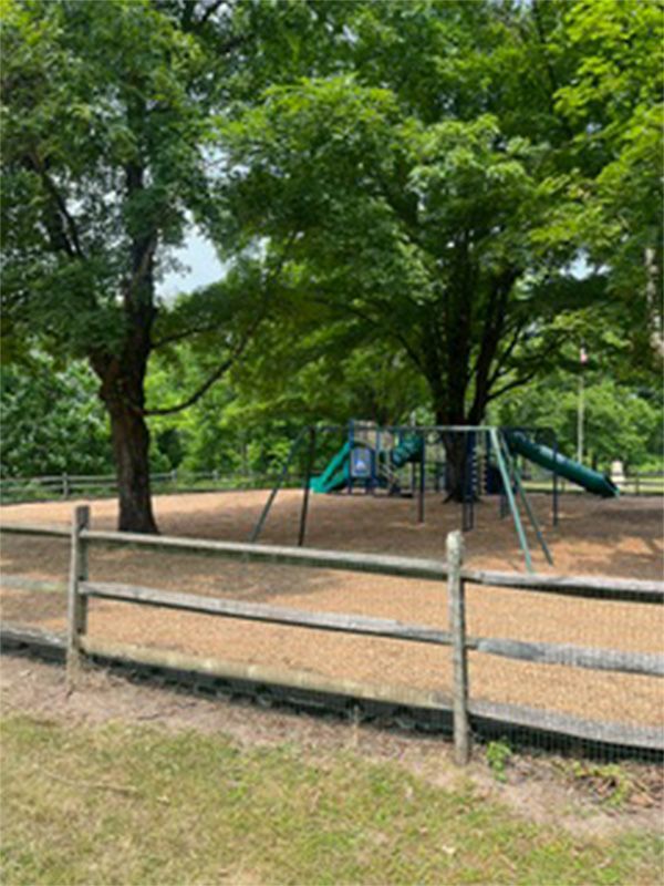 A wooden fence surrounds a playground in a park.