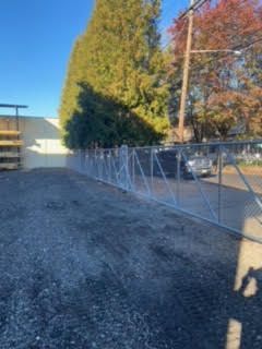 A chain link fence is sitting on the side of a gravel road.