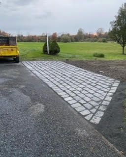 A yellow truck is parked on the side of a road next to a brick driveway.