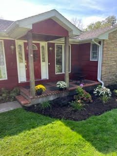 A red house with a porch and flowers in front of it.