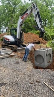 A man is standing next to a large concrete block being lifted by an excavator.