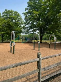 A playground with a wooden fence and trees in the background.