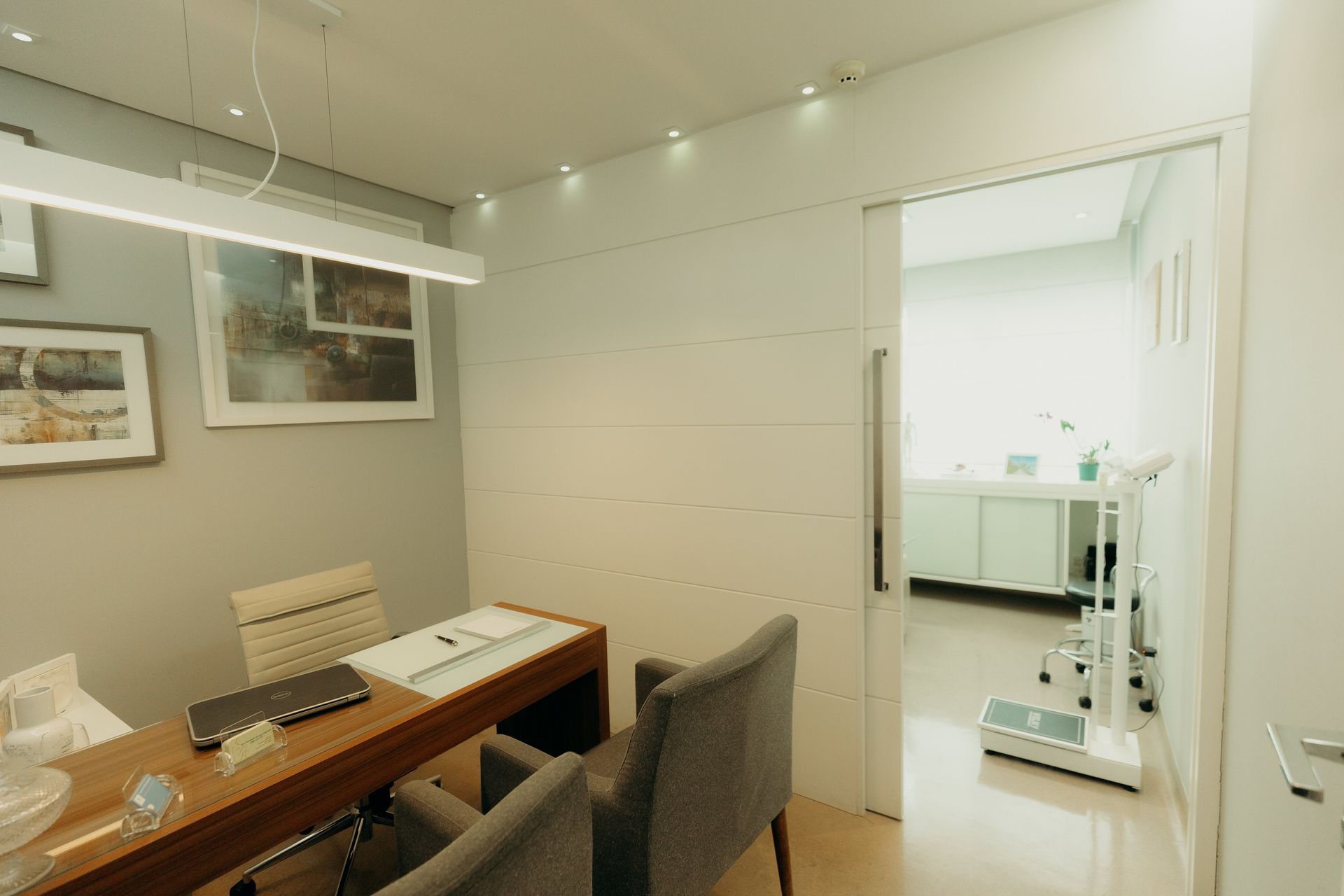 Um consultório médico com uma mesa, cadeiras e uma balança.