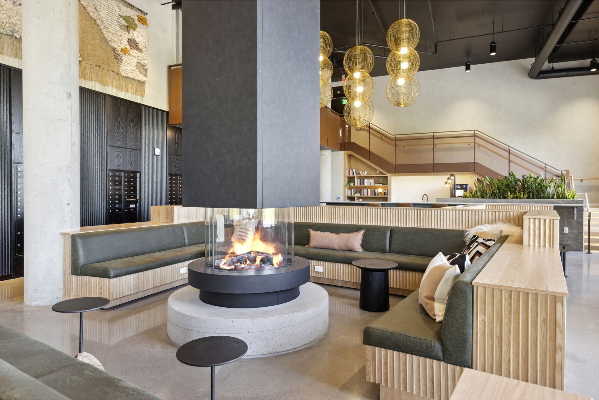 Warm modern lobby with a circular fireplace, curved green couches, and a staircase at Esox House in St. Paul, MN.