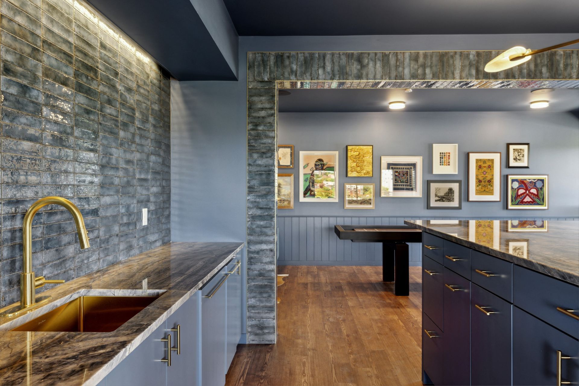 Blue kitchen with marble countertops, brass faucet, and an art gallery wall in the adjacent room at Esox House in St. Paul, MN.