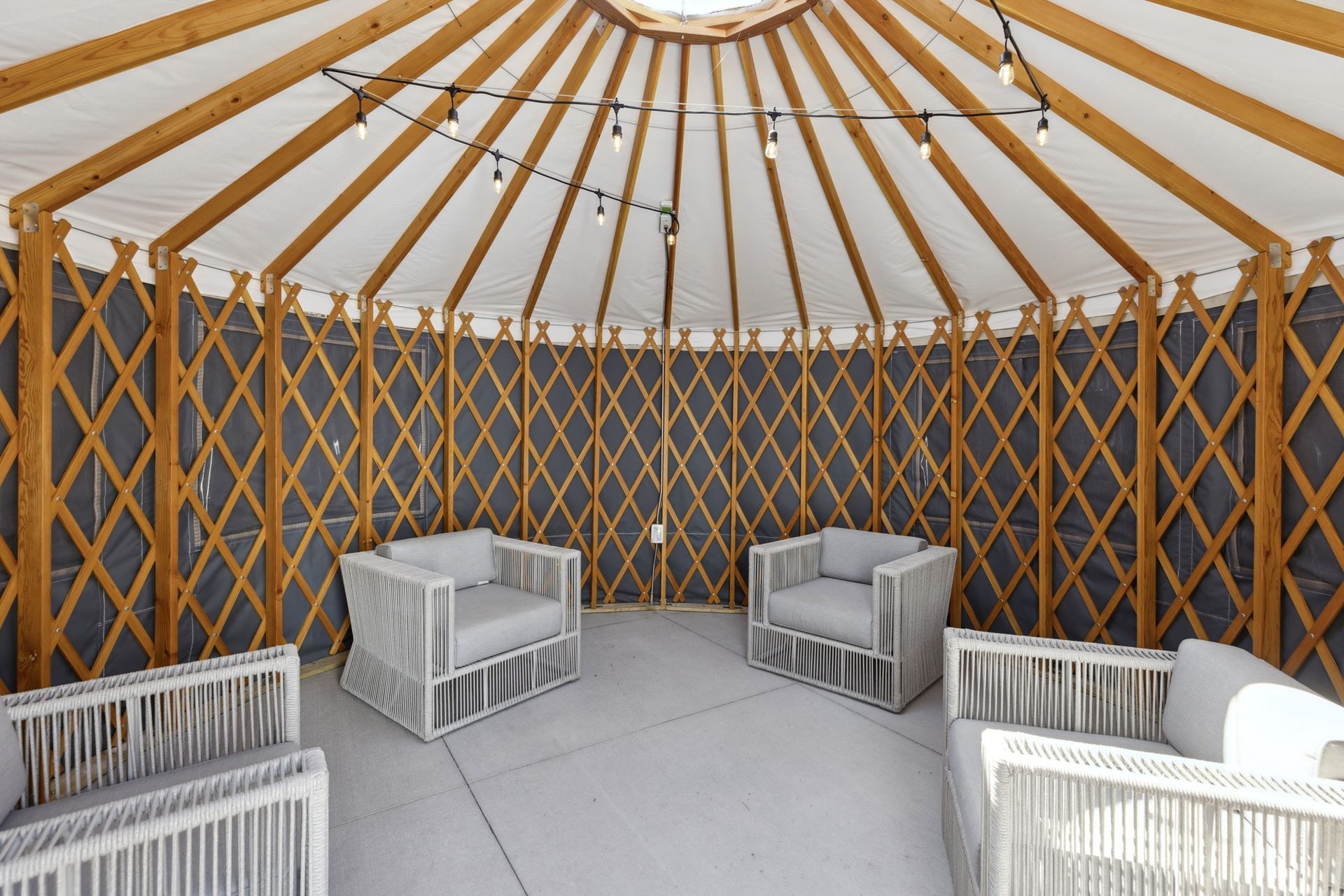 Interior of a wooden lattice tent with string lights and gray outdoor lounge chairs at Esox House in St. Paul, MN.